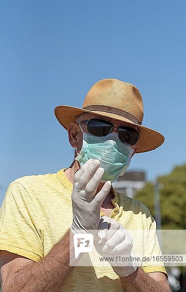 Southsea  Portsmouth  Südengland  UK. Mai 2020. Mann mit Maske  der während des Ausbruchs von Corvid-19 medizinische Gummi-Schutzhandschuhe anzieht. Am Strand von Southsea.