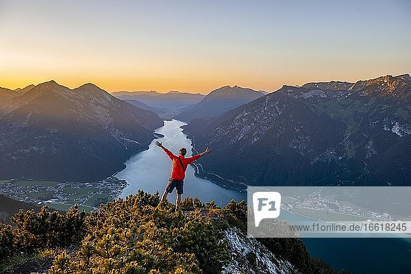 Sonnenuntergang  junger Mann streckt die Arme in die Luft  Ausblick vom Gipfel des Bärenkopf auf den Achensee  links Seebergspitze und Seekarspitze  rechts Rofangebirge  Tirol  Österreich  Europa