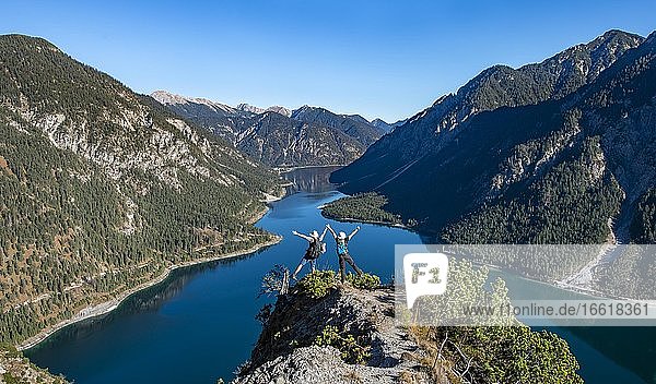Two hikers stretch arms in the air  view of Plansee  Schönjöchl in the background  hike to the Schrofennas  Ammergau Alps  Reutte district  Tyrol  Austria  Europe