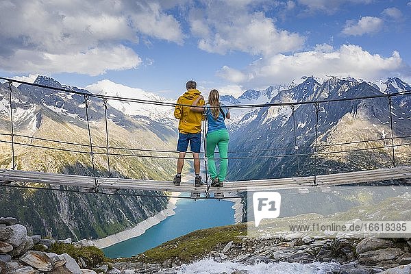 Wanderer  junge Frau und junger Mann auf Hängebrücke an der Olpererhütte  Ausblick auf Schlegeisstausee  Speicher Schlegeis  hinten Zillertaler Alpen mit Gletscher Schlegeiskees  Zillertal  Tirol  Österreich  Europa
