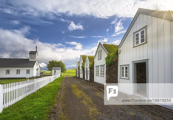 Weiße Häuser mit Grasdach und Steinmauer an einem Schotterweg  Kirche mit weißem Zaun auf Torfhof  Grassodenhaussiedlung Grenjadarstadur  Grenjaðarstaður  Þingeyjarsveit  Norðurland eystra  Island  Europa