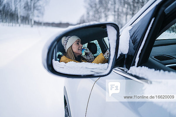 Reife Frau  die im Auto über ein Mobiltelefon spricht und sich im Seitenspiegel spiegelt
