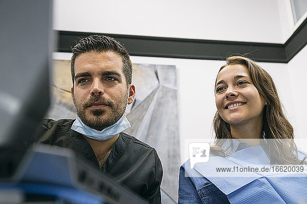 Schöne Patientin freut sich über die Erklärungen eines gutaussehenden männlichen Zahnarztes am Laptop in der Klinik