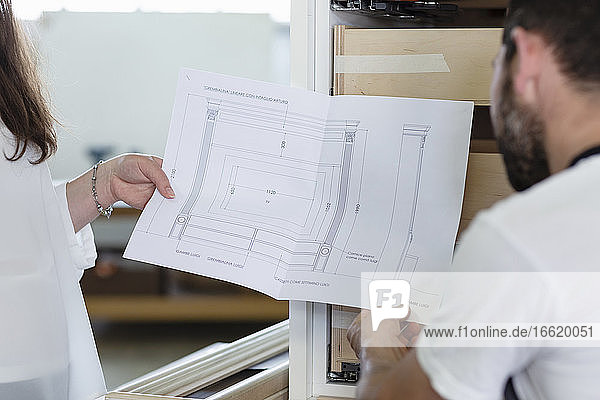 Innenarchitekt zeigt einem Tischler in der Werkstatt den Entwurf einer Schublade