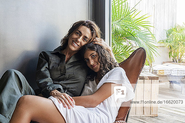 Lächelnde Mutter und Tochter  die sich umarmen  während sie auf einem Stuhl zu Hause sitzen