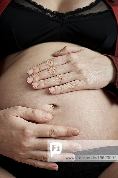 Nahaufnahme einer schwangeren Frau mit Händen auf dem Bauch  die zu Hause sitzt