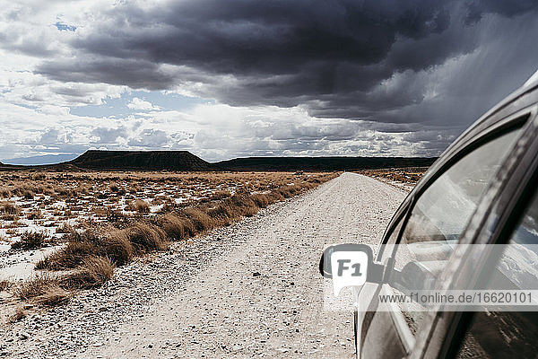 Spain  Navarre  Storm clouds over car driving along empty dirt road in Bardenas Reales