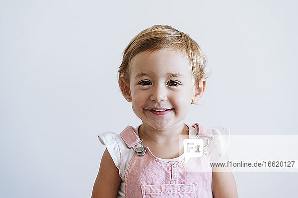 Lächelndes kleines Mädchen  das an einer weißen Wand steht