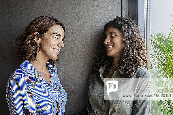 Mother and daughter talking while leaning on wall at home