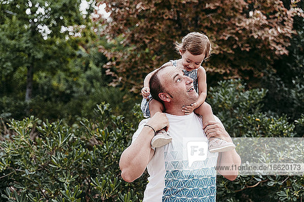 Father carrying daughter on shoulder while standing in park