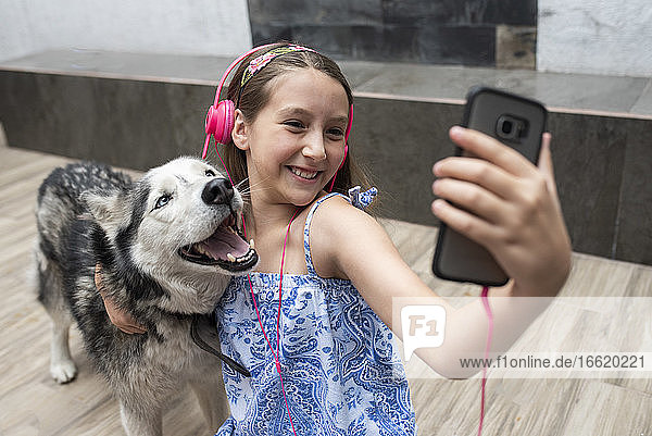 Smiling girl taking selfie with dog while sitting on floor at home