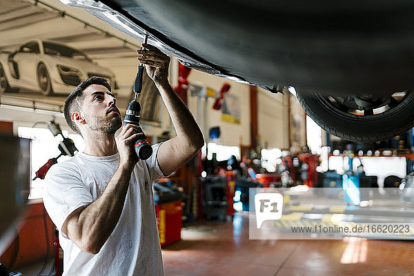 Young mechanic repairing car with work tool in auto repair shop