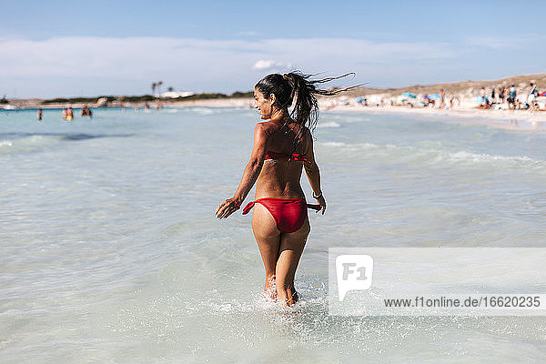 Glückliche Frau im Bikini geht im Meer gegen den Himmel
