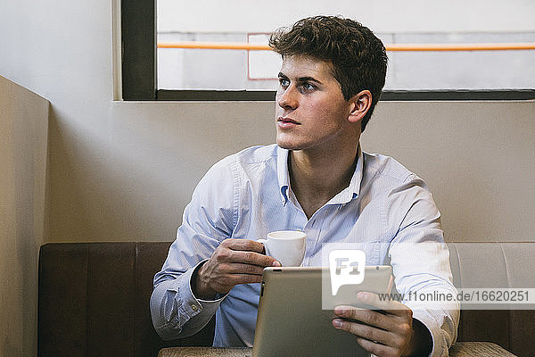 Gut aussehender junger Mann mit Kaffeetasse und digitalem Tablet  der in einem Café sitzt