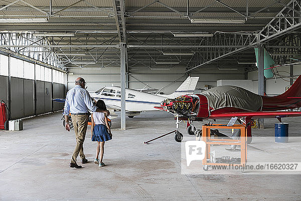 Enkelin und Großvater gehen in einem Flugzeughangar spazieren