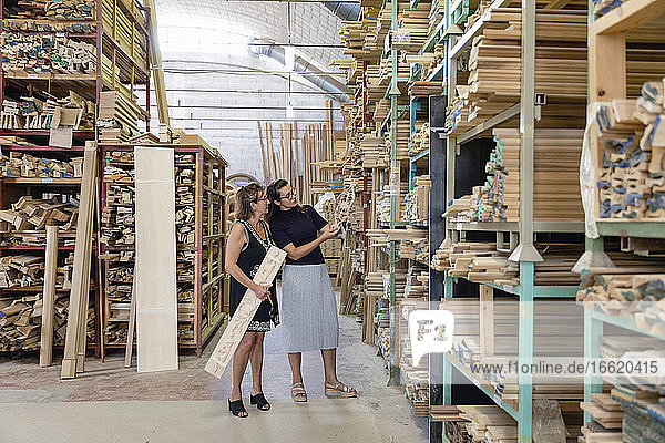 Frauen wählen eine verzierte Holzplatte aus  während sie in einem Lagerhaus in einer Fabrik stehen