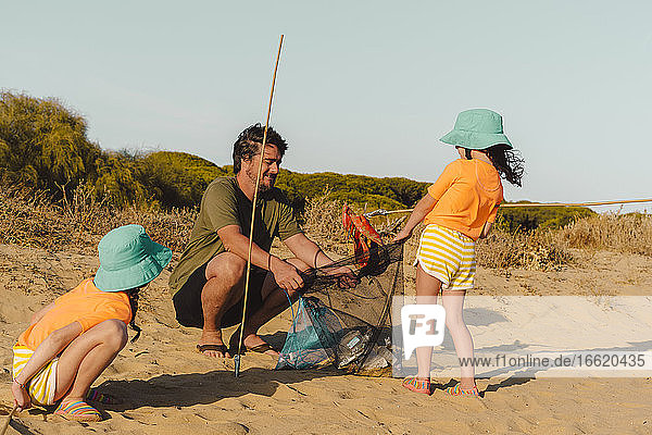 Vater und Töchter beim Müllsammeln am Strand