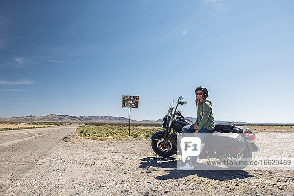 Frau auf Motorrad sitzend an einer Wüstenstraße gegen den Himmel während einer Autoreise  Nevada  USA