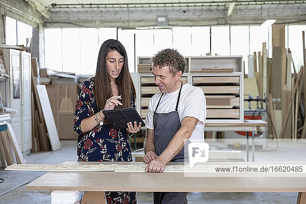 Ein Innenarchitekt zeigt einem Schreiner in der Werkstatt ein digitales Tablet