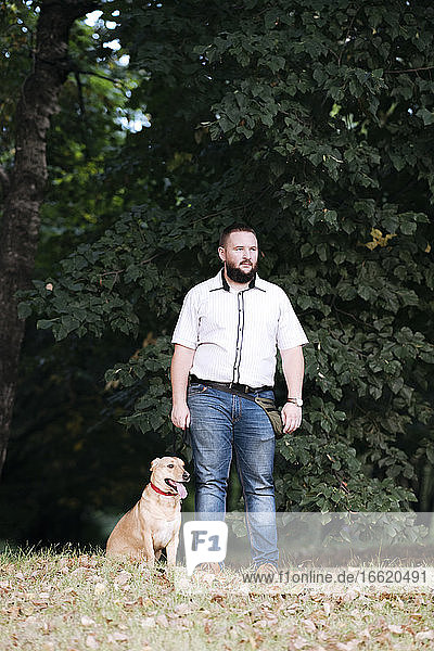 Mid adult man looking away while standing with dog in park