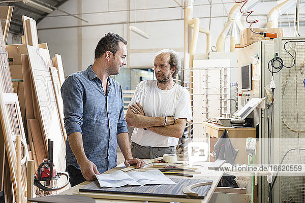 Smiling project manager talking with coworker while standing in factory