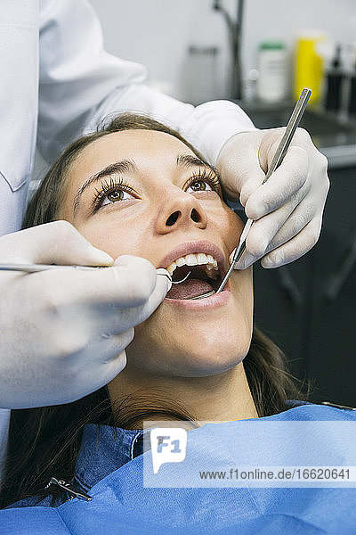 Zahnarzt mit Handschuhen bei der Untersuchung der Mundhöhle eines hübschen Patienten in einer Klinik