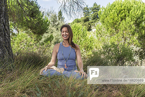 Lächelnde Frau übt Yoga  während sie unter einem Baum im Gras sitzt