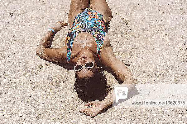 Mid adult woman wearing bodysuit lying at Valdevaqueros beach on sunny day  Tarifa  Spanien