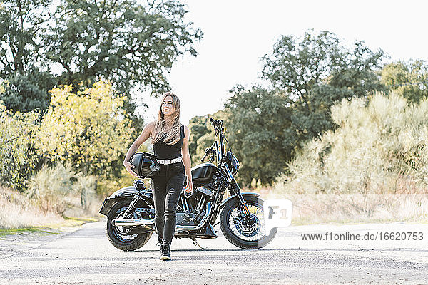 Schöne Motorradfahrerin  die auf der Straße gegen ein Motorrad läuft und wegschaut
