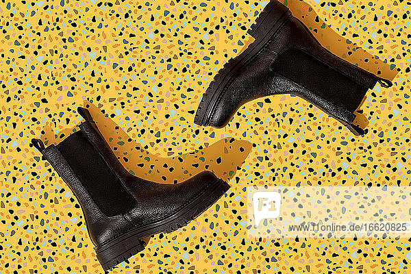 Pair of black leather boots on yellow terrazzo pattern