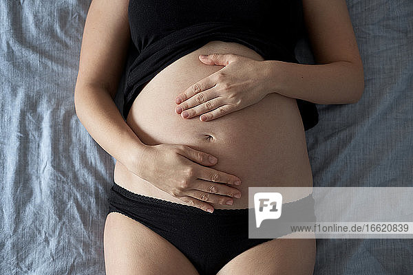 Schwangere Frau berührt den Bauch  während sie zu Hause auf dem Bett liegt