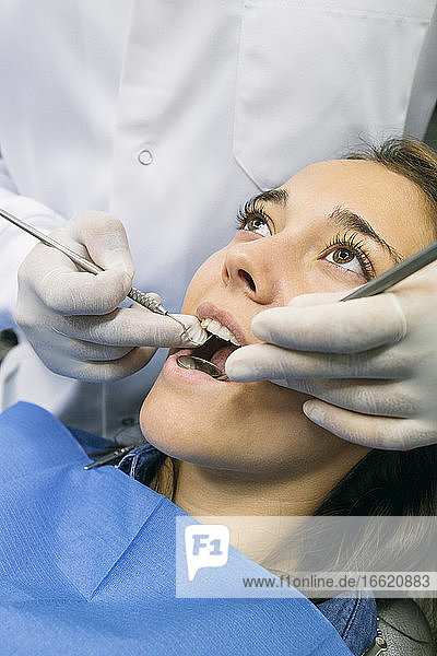 Zahnarzt mit Handschuhen bei der Untersuchung der Mundhöhle einer Patientin in einer Klinik
