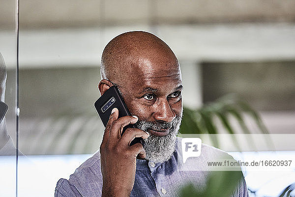 Lächelnder  selbstbewusster Geschäftsmann  der einen Anruf über sein Smartphone entgegennimmt