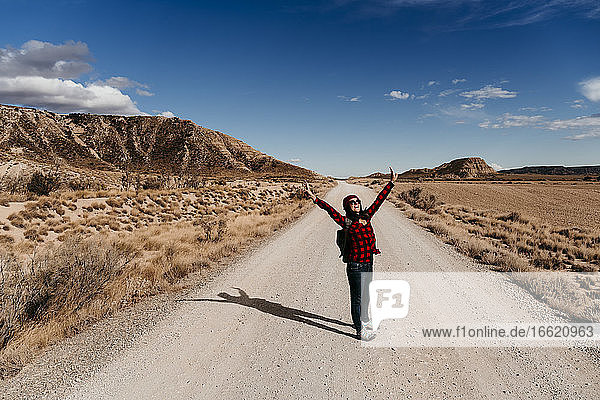 Spain  Navarre  Female tourist standing with raised arms in middle of empty dirt road in Bardenas Reales