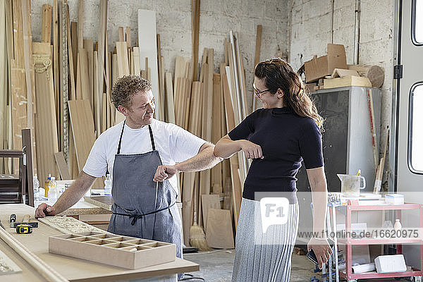 Smiling man and woman giving elbow bump while standing at workshop