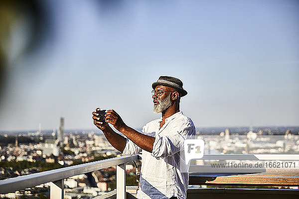 Älterer Mann  der ein Selfie macht  während er ein Smartphone benutzt  das auf einer Gebäudeterrasse steht
