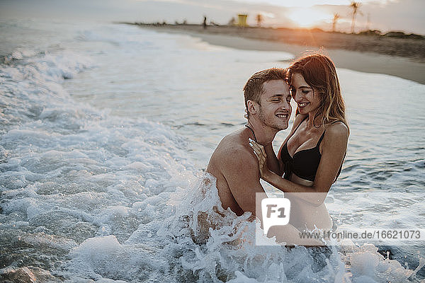 Smiling couple enjoying while sitting in water at beach