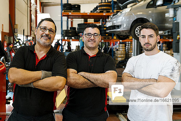 Confident male coworkers with arms crossed standing in auto repair shop