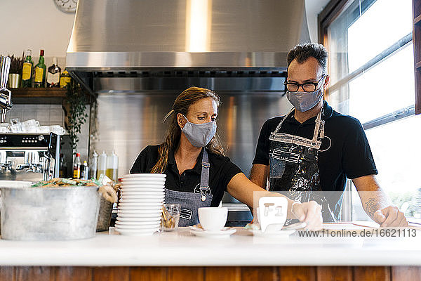 Männliche und weibliche Baristas mit Schutzmaske bei der Arbeit in einem Café während COVID-19