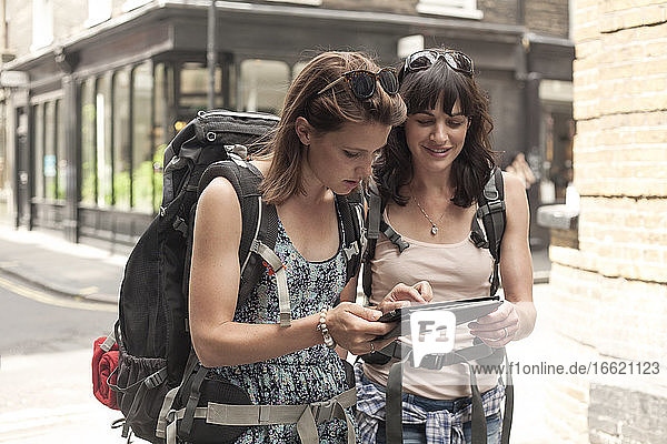Weibliche Rucksacktouristen nutzen ein digitales Tablet als Orientierungshilfe bei der Erkundung der Stadt