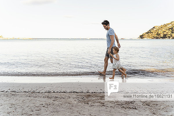 Glücklicher Vater  der mit seiner Tochter am Strand spazieren geht