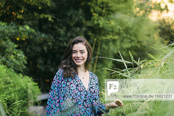 Lächelnde schöne Frau steht inmitten von Pflanzen im Park
