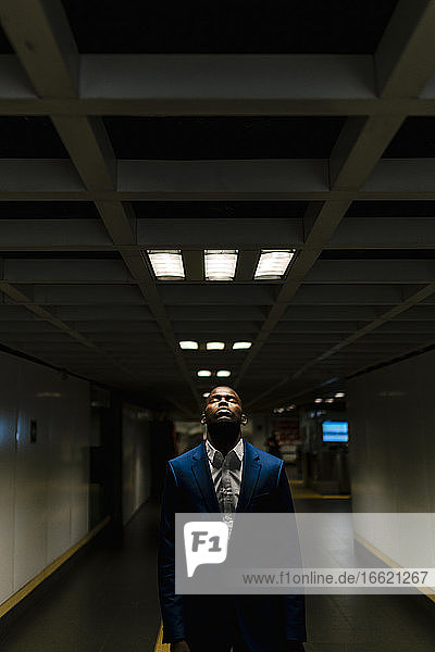 African businessman with eyes closed standing under illuminated light in subway