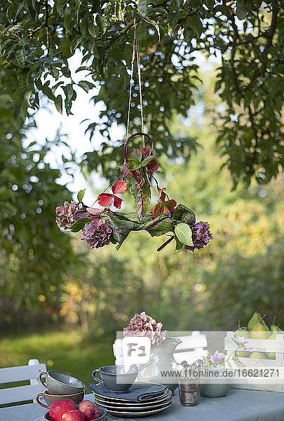 Lampenschirm aus Blättern und blühenden Hortensien hängt über einem Couchtisch im Garten