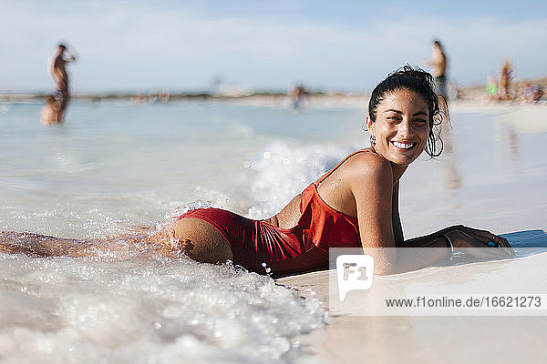 Lächelnde erwachsene Frau in Dessous am Strand liegend gegen den Himmel