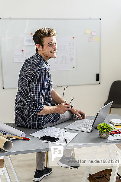 Man smiling while sitting on desk at office