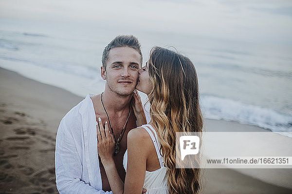 Junge Frau küsst Mann am Strand stehend