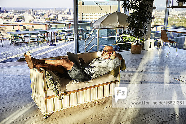 Mature man lying down while using laptop at home