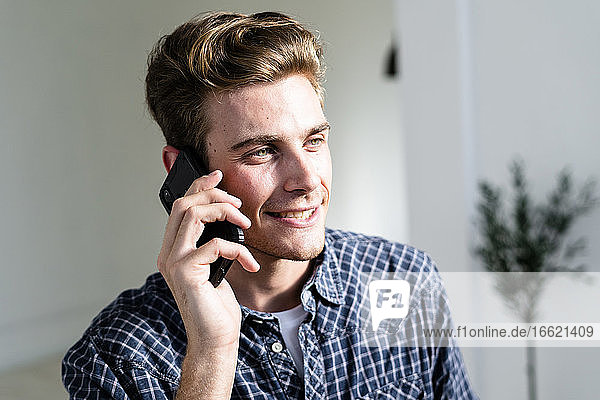 Lächelnder Mann  der im Büro steht und mit seinem Handy spricht