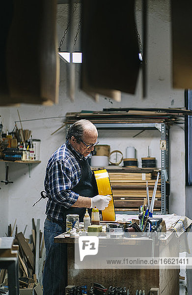 Craftsman making guitar while standing at workshop
